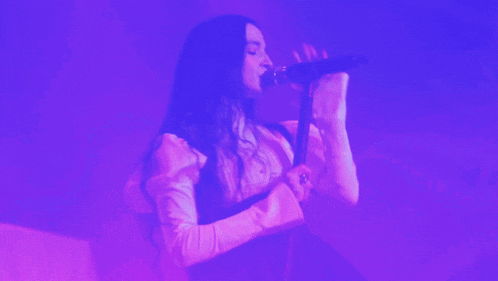 a woman is singing into a microphone in a purple light