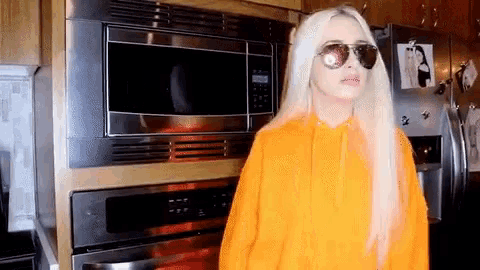 a woman wearing sunglasses stands in front of a microwave oven