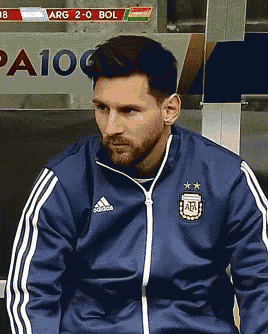 a man wearing a blue adidas jacket sits in a locker room