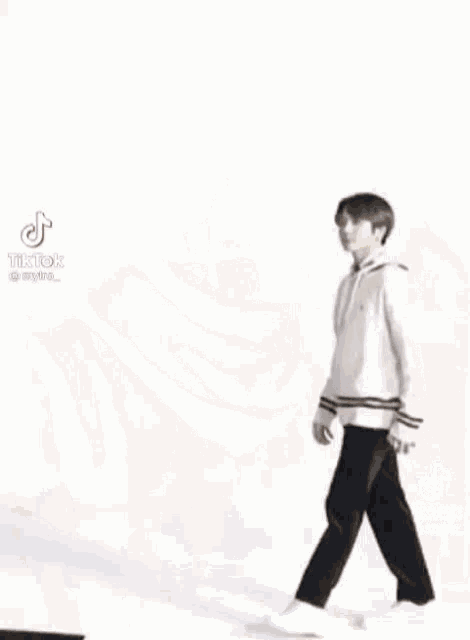 a young man wearing a white sweater and black pants is walking .