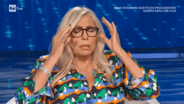a woman wearing glasses has her hands on her head while sitting on a rai tv show