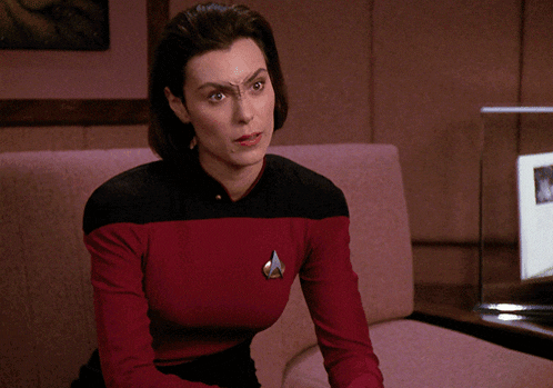 a woman sitting on a couch wearing a red and black shirt with a star trek logo on her chest