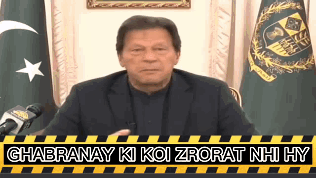 a man in a suit stands in front of microphones with the words ghabranay ki koi zorat nhi hy written below him