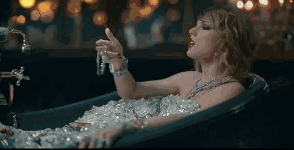 a woman is laying in a bathtub covered in ice holding a necklace .