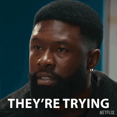 a man with a beard is making a funny face and saying they 're trying .