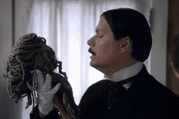a man in a tuxedo and bow tie is holding a mop in his hand .