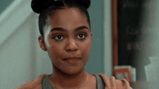 a young girl with a bun in her hair is looking at the camera with a serious look on her face .