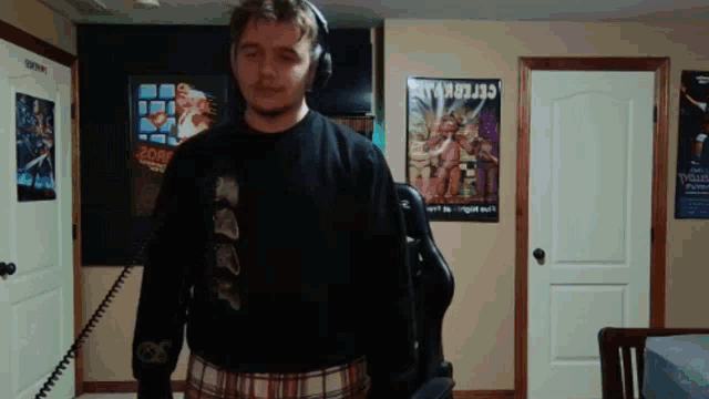 a man wearing headphones stands in a room with posters on the wall including one that says zork