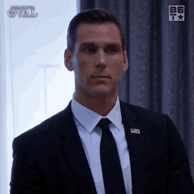 a man in a suit and tie stands in front of a sign that says be i