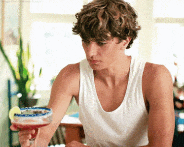 a man in a white tank top holds a margarita in his hand