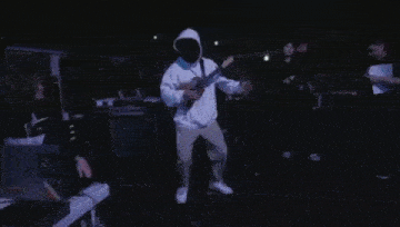 a man in a hoodie playing a guitar in a dark room
