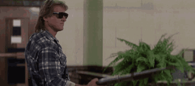 a man in a plaid shirt and sunglasses holds a gun