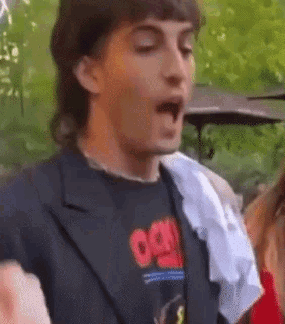 a man with a mullet is wearing a black jacket and a black t-shirt with the word oasis on it .