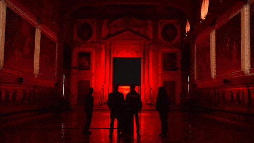 a group of people standing in a dark room with a red light
