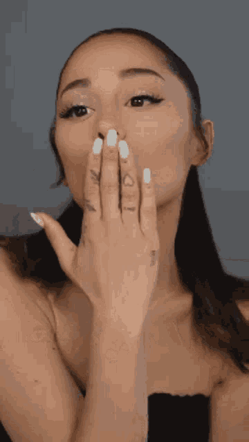 a woman with white nails is blowing a kiss with her hand covering her mouth .