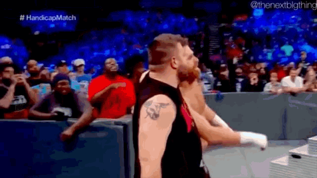 a man with a tattoo on his arm is standing in front of a crowd during a wrestling match .