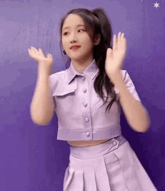 the girl is wearing a purple crop top and a purple skirt and is dancing .