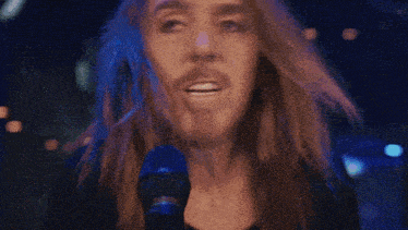 a man with long hair and a beard is singing into a microphone with the words " did you r " behind him