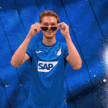 a man wearing sunglasses stands with his arms crossed in front of a blue background
