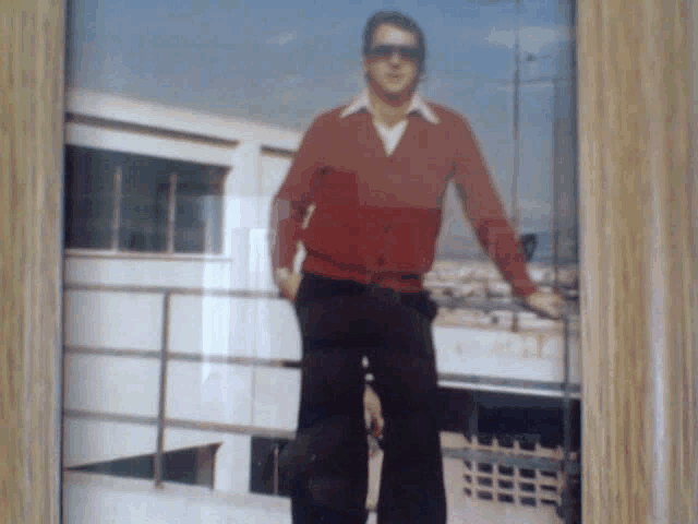 a man wearing sunglasses and a red sweater is standing on a balcony