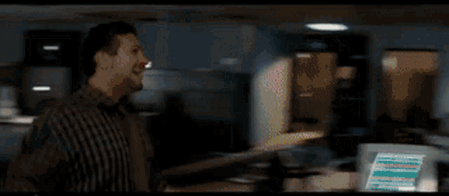 a man in a plaid shirt is smiling in front of a computer monitor