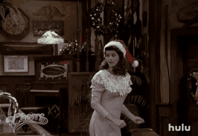 a woman in a santa hat is standing in front of a sign that says hulu