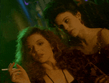 a woman smoking a cigarette next to another woman in a green light