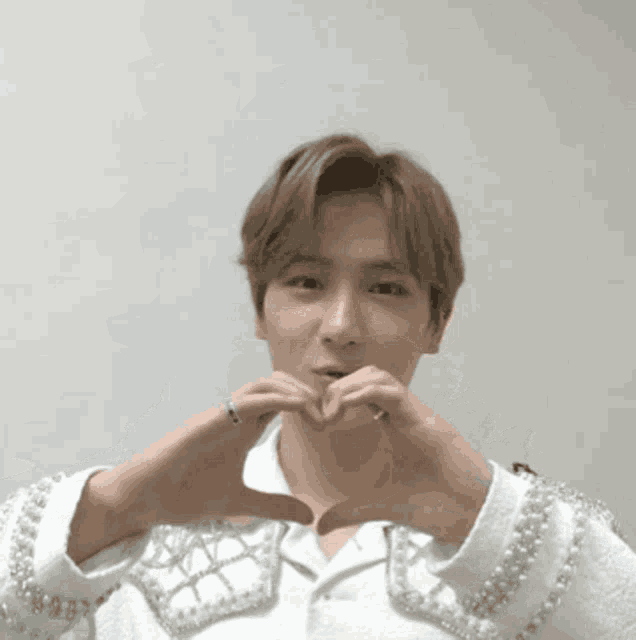 a man wearing a white shirt with pearls on the sleeves is making a heart shape with his hands