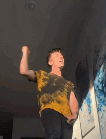 a man in a yellow and black tie dye shirt is standing on a wall .