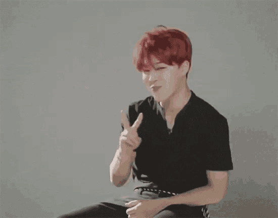 a man with red hair is sitting down and making a peace sign .