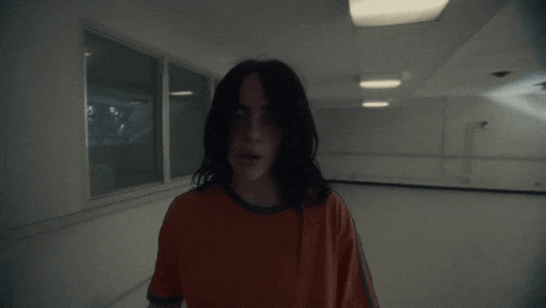 a woman in an orange shirt is standing in a dark room