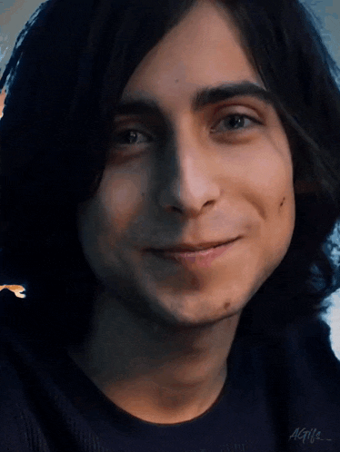 a close up of a young man with long hair smiling
