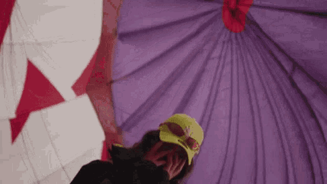 a woman wearing a yellow hat and sunglasses is standing inside of a purple hot air balloon .