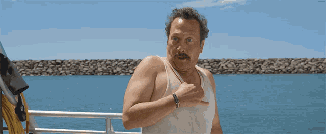 a man in a white tank top is standing on a boat in the water