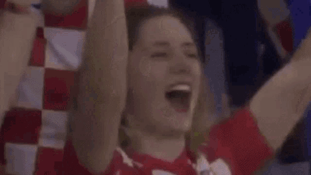 a woman in a red and white checkered shirt is raising her arms in the air with the word gopic above her head .