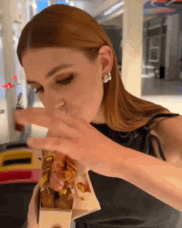 a woman with long red hair is eating a sandwich from a box