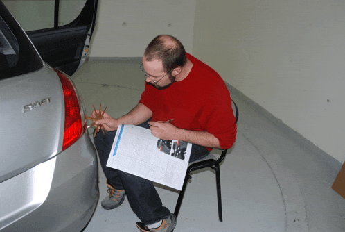 a man sits in front of a silver car with the word swift on the back