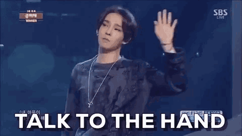 a man is standing on a stage with his hand up and the words `` talk to the hand '' written on the screen behind him .