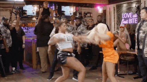 two women are dancing in front of a neon sign that says love at last bite