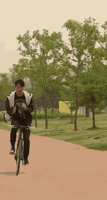a man wearing a black shirt that says captain on it is riding a bike down a path