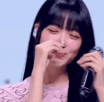 a girl with long black hair is holding a microphone in her hand and covering her nose .