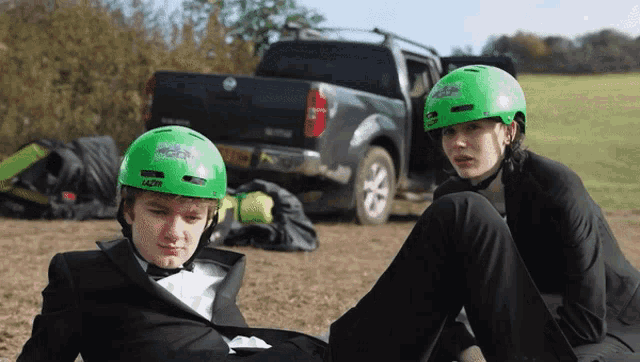 a boy wearing a green helmet that says lazer sits next to another boy