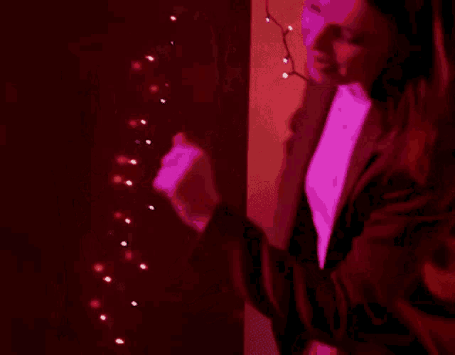 a woman in a red jacket and white shirt is dancing in a room with purple lights .