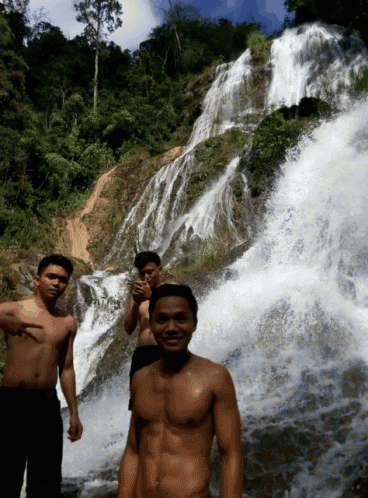 a shirtless man stands in front of a waterfall