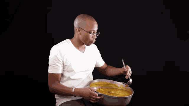 a man in a white shirt is eating soup from a bowl with a spoon