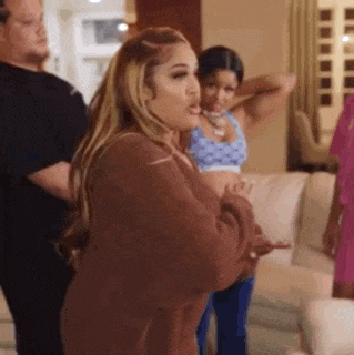 a woman in a brown sweater is standing in a living room with other women .