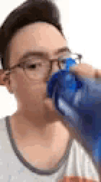 a young man is drinking water from a blue bottle .