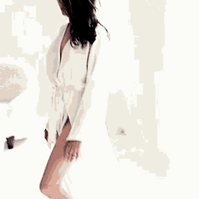a woman in a white robe is standing on a bed in a room .