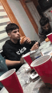 a man wearing a black hoodie with the word acids on it is eating a sandwich