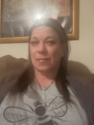a woman wearing a shirt with a bee on it is sitting in front of a framed picture